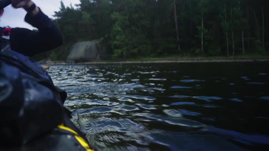 A closeup view of a persons arm paddling a kayak in a lake near a forest