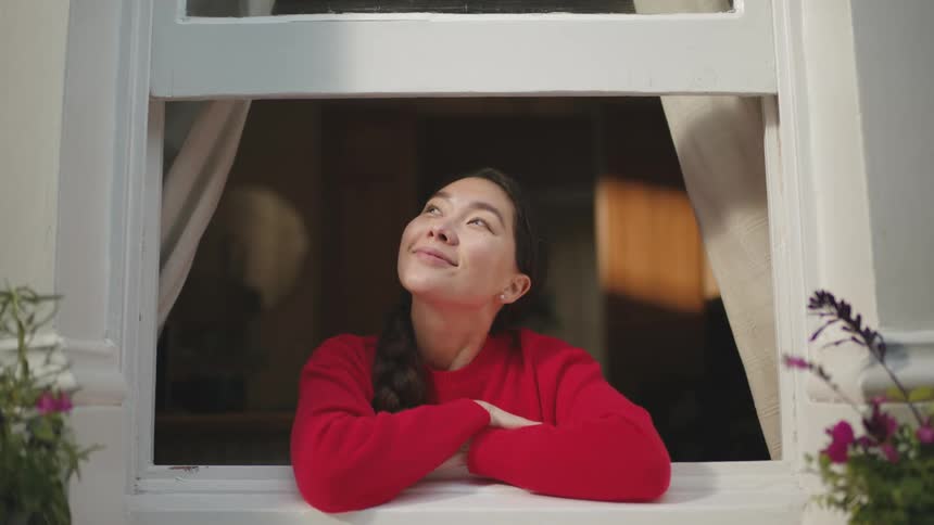 Young woman opening the white curtain of a window and looking smiling
