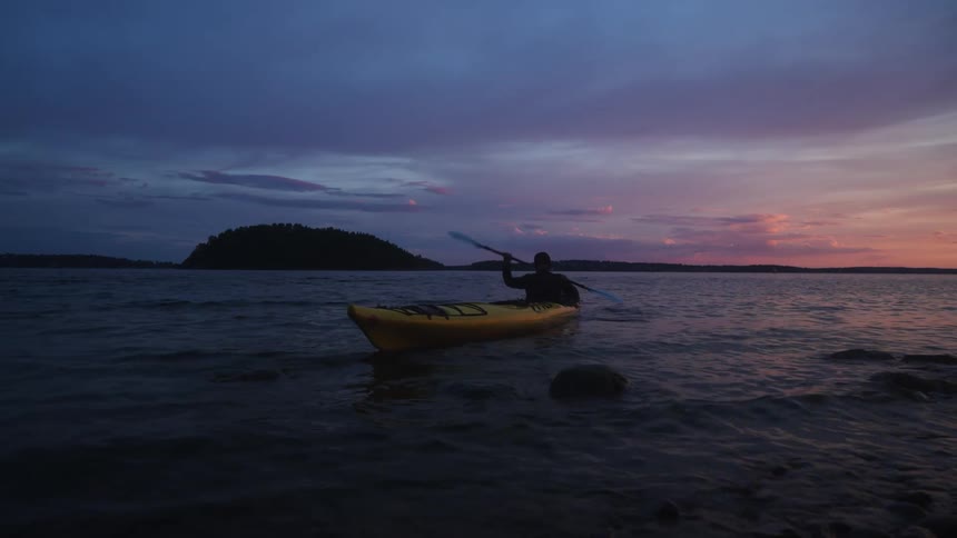 A person kayaking near the rocky shore during sunset