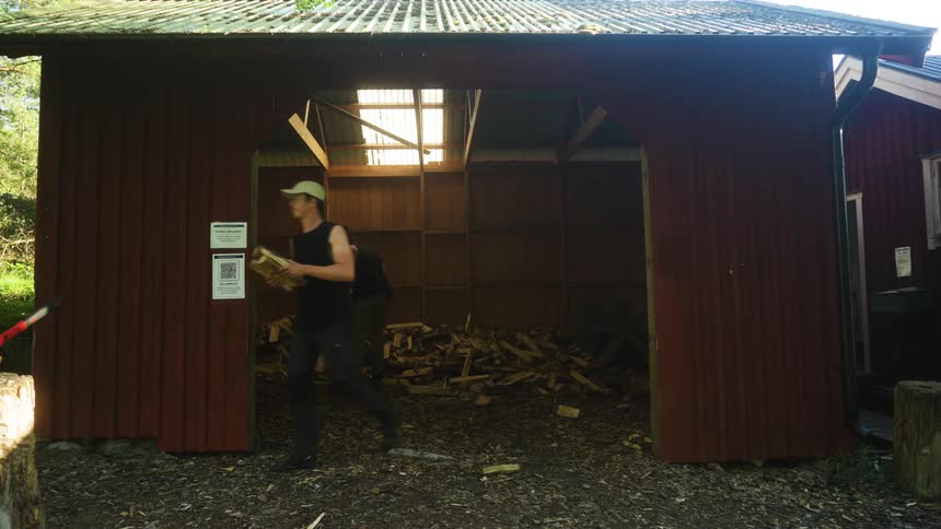 Red wooden shed open and two men coming out with firewood