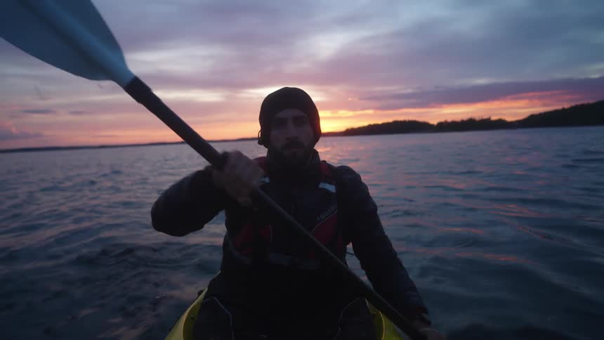 Man paddling a yellow kayak on a lake at sunrise