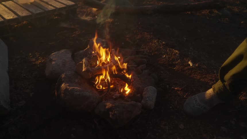Hand throwing a log into a fire burning on the ground
