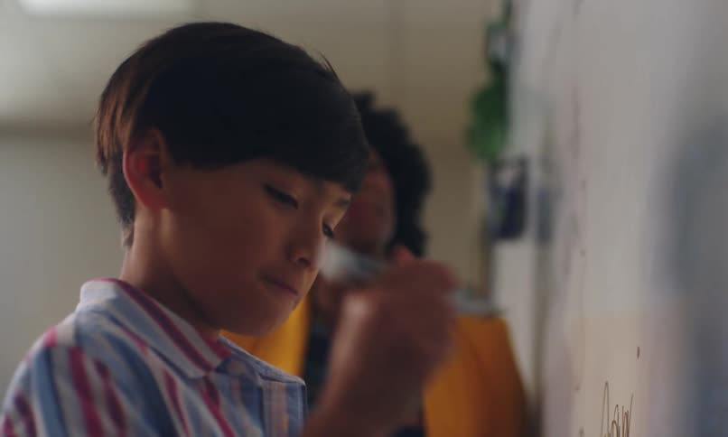 Teacher handing a pen to a boy writing on the whiteboard in the classroom