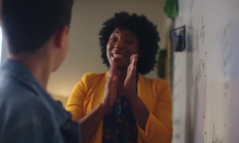 A student solves a math problem on a whiteboard and the teacher congratulates him