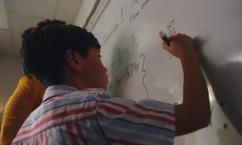 A teacher helping a student with a math problem on a whiteboard