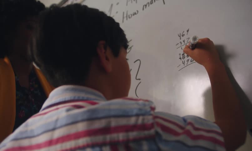 Teacher guides a student while he solves a math problem on the white board