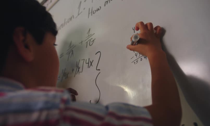 Student solving a math problem on the white board as teacher advises him