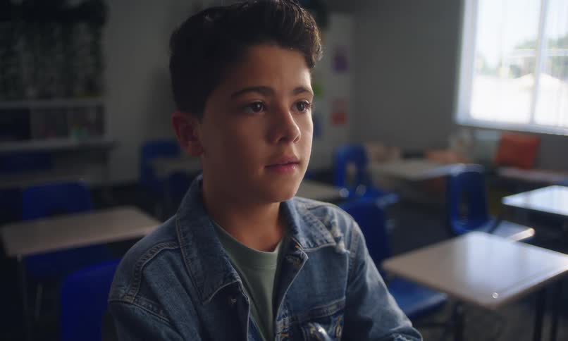 A young student sits at a desk in a classroom verbally answering questions