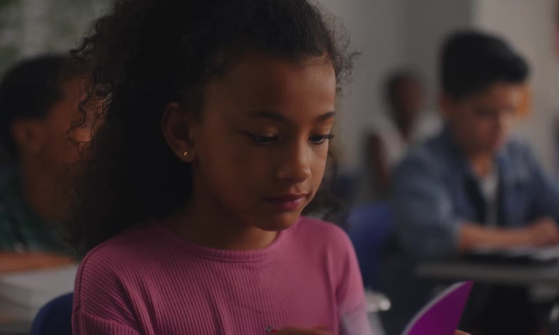 A young girl with curly hair focused on her work in a classroom setting