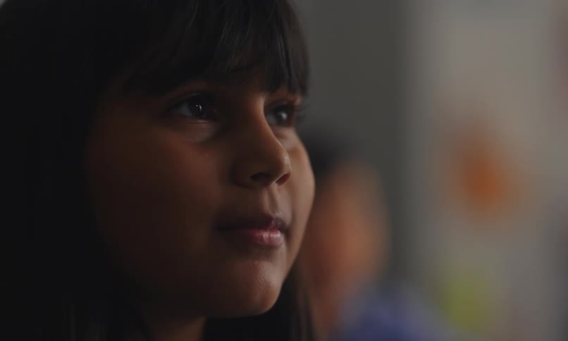 The face of a little girl who has a small smile and she is looking forward