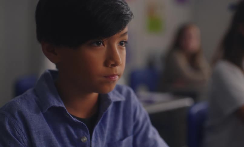 Boy in a classroom looking forward and down while sitting