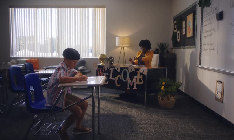 In a classroom a student solves a test while the teacher glances at her watch