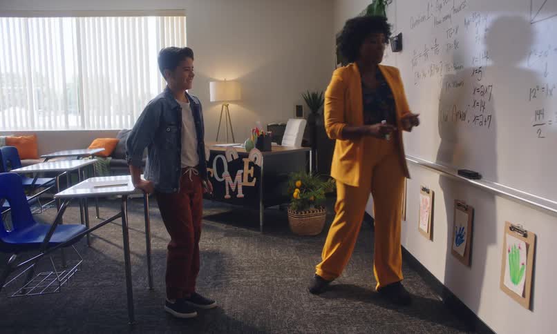 Teacher solving a math problem on a whiteboard and talking to a student in a classroom