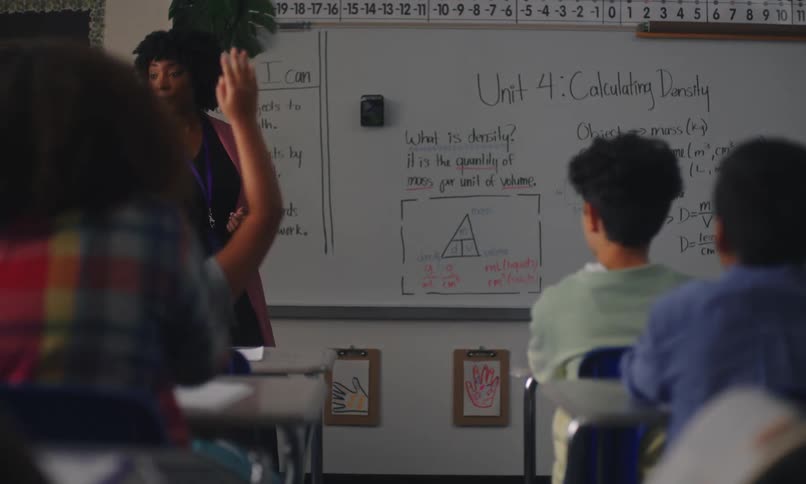 A teacher in a classroom discussing a lesson on calculating density with students attentively listening
