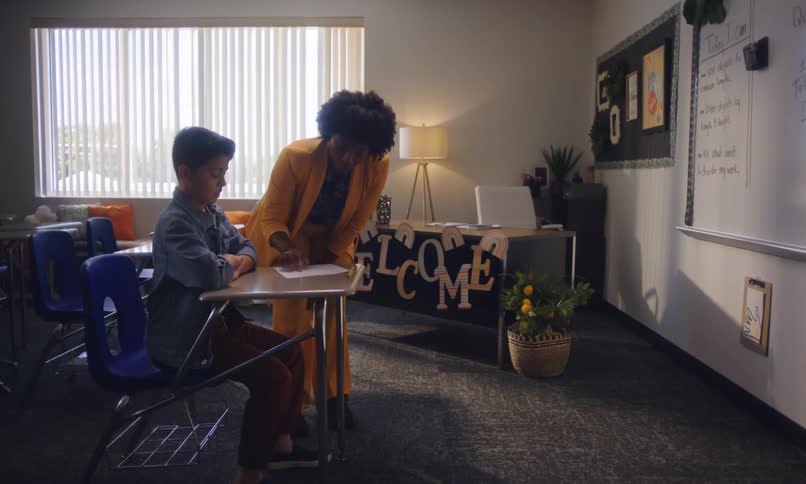 In a classroom a student solves a test while congratulates him for his great results