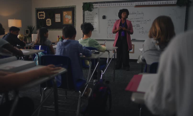Teacher in a class of students in the classroom talking to students who raise their hands