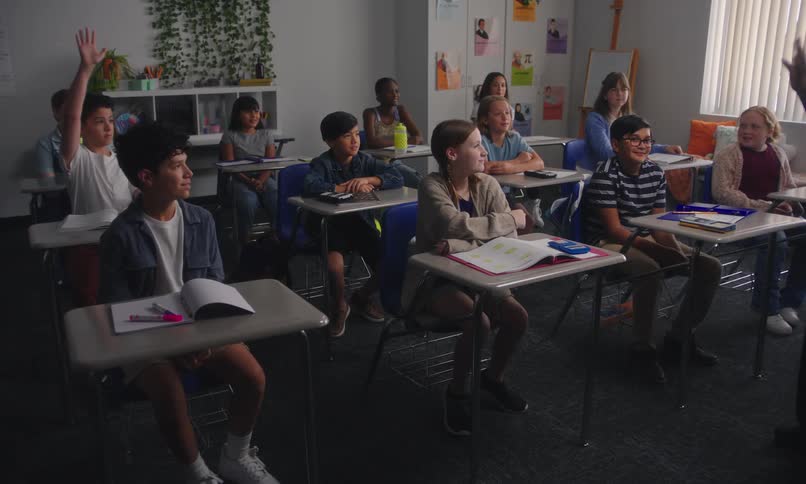 A classroom with students seated at desks facing a teacher standing at the front