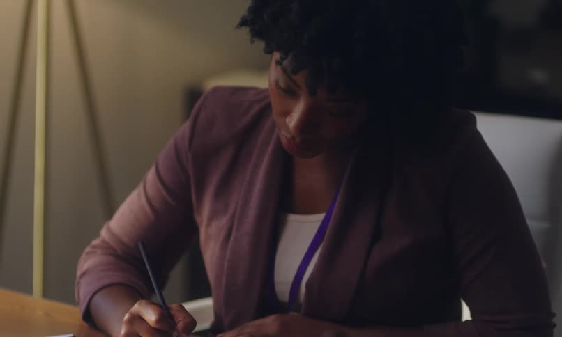 An individual sits at a desk diligently writing in a notebook with a pencil