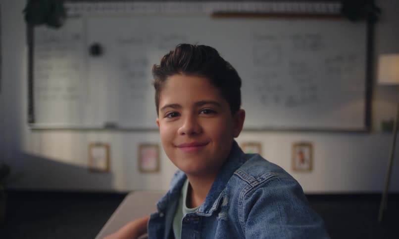 A boy in a denim jacket sits in front of a whiteboard in the classroom