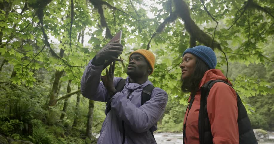 Two hikers standing next to a stream in the forest take pictures with a tablet