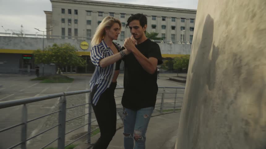 A couple dances outside alongside a concrete structure