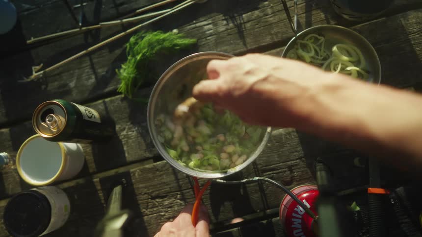 A person is cooking a pan of vegetables on a wooden table top