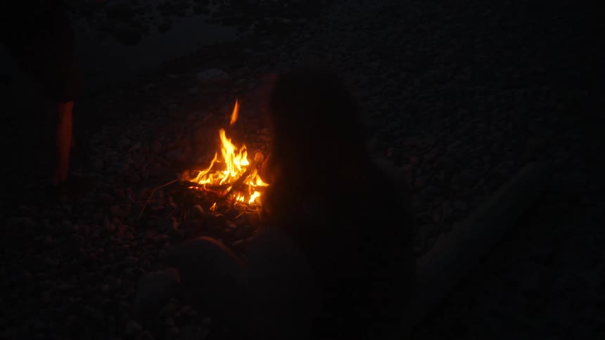 Sillhouette of a person sitting near a campfire during twilight or night time