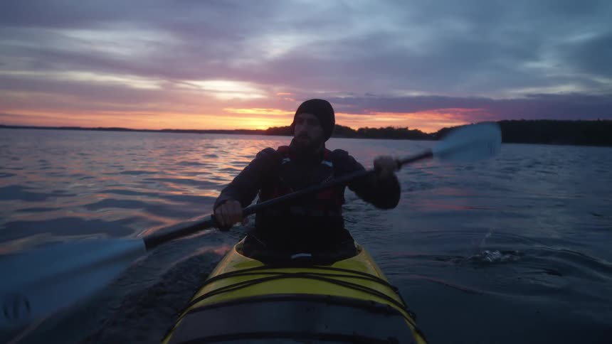 Silhouette of a man paddling a kayak on a lake at sunrise or sunset