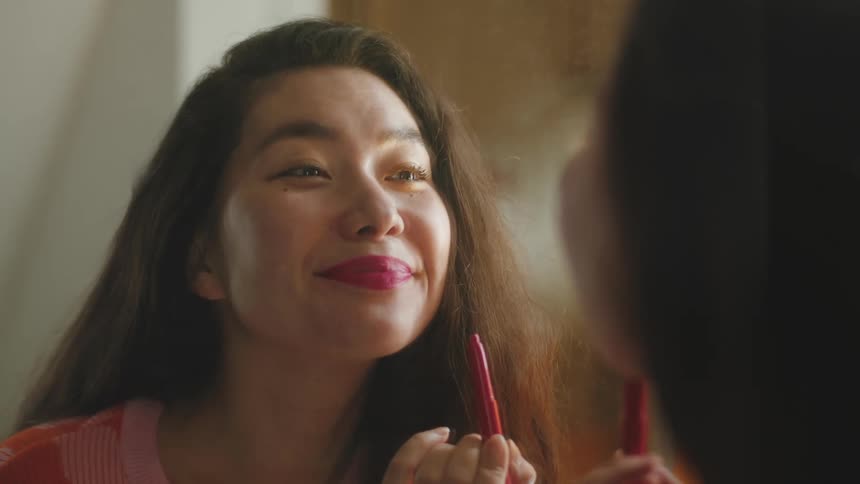 A young woman putting on red lipstick while looking at herself in the mirror and then she walks away