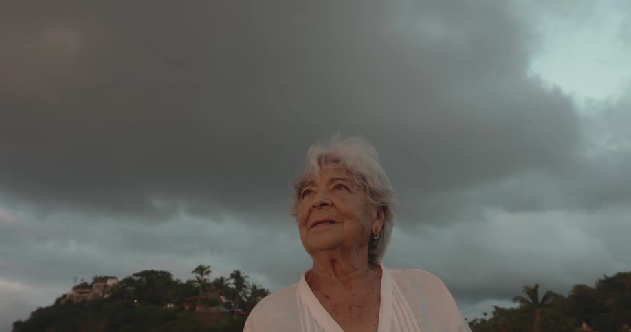 A lady is looking forward and behind her the sky with big gray clouds