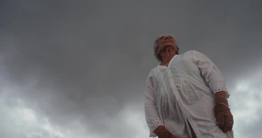 An elderly woman standing against a dramatic cloudy sky