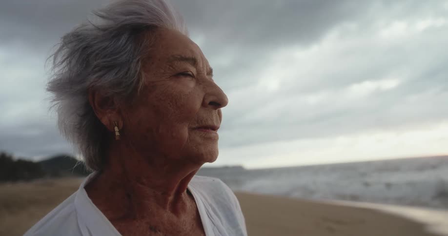Close up of an elderly woman wind blowing on her face standing next to a beach