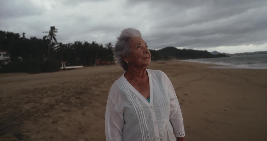 Close up of an elderly woman wind blowing on her face standing next to a beach