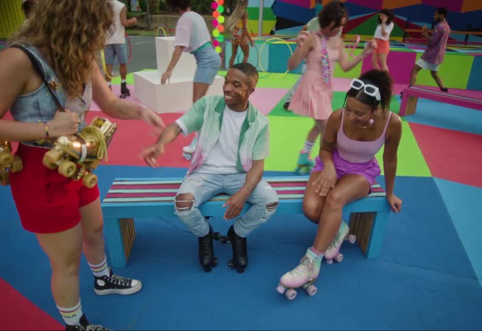 A group of young people talk and engage with roller skating and dancing in the background