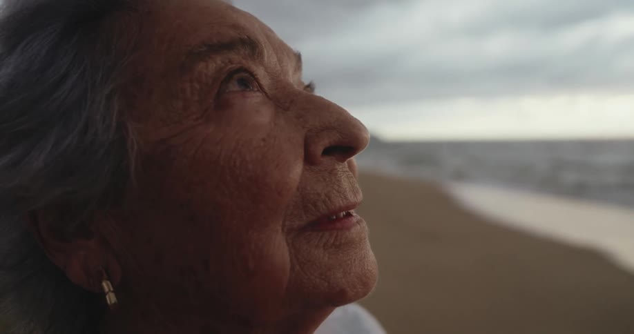 Close up of an elderly woman wind blowing on her face standing next to a beach