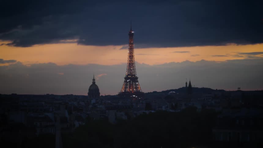 Eiffel tower illuminated at dusk with a sunset sky in shades of yellow and blue in the background