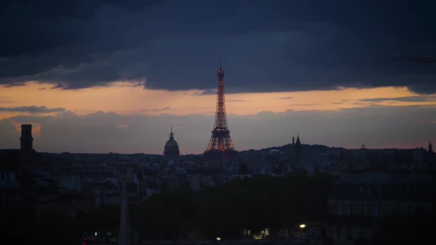 Eiffel tower at dusk illuminated against the cloudy sky with city buildings in the foreground