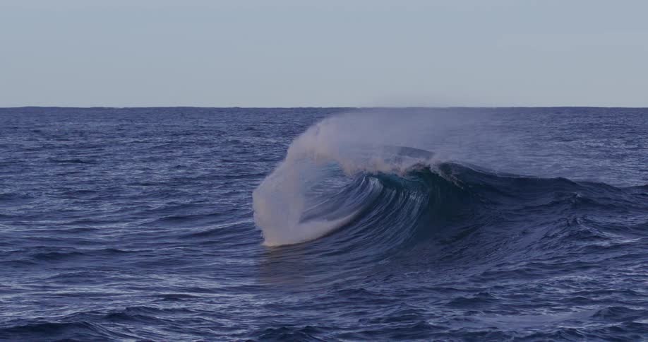Large wave breaks creating a spray of white water on a cloudy day