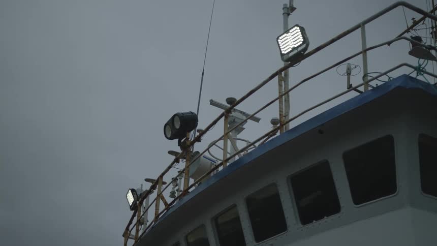 Front and top of a boat with reflective lights against a cloudy sky