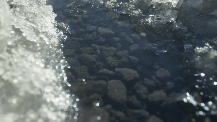 Snow and ice lining a stream melts in the sunlight