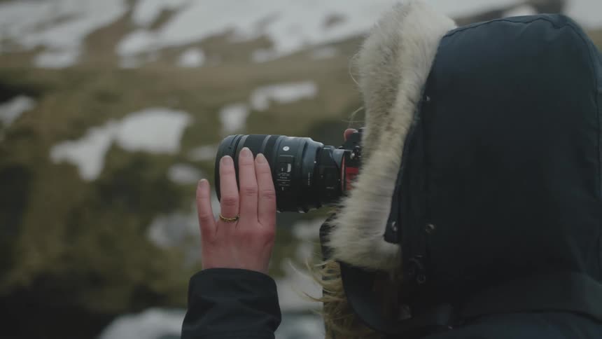 Female photographer standing on the snowy shore during winter uses a telephoto lens