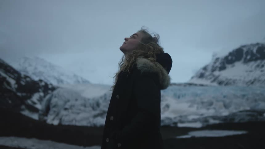 A woman is looking up at the sky by the mountain