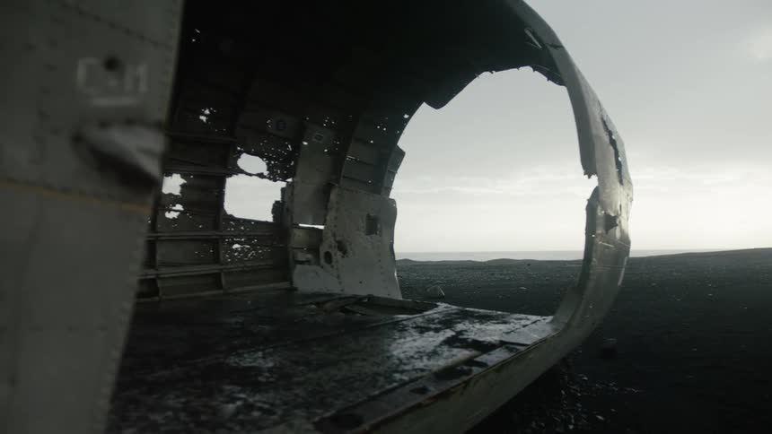 Dilapidated airplane fuselage overlooking a dark stony lake under a cloudy sky