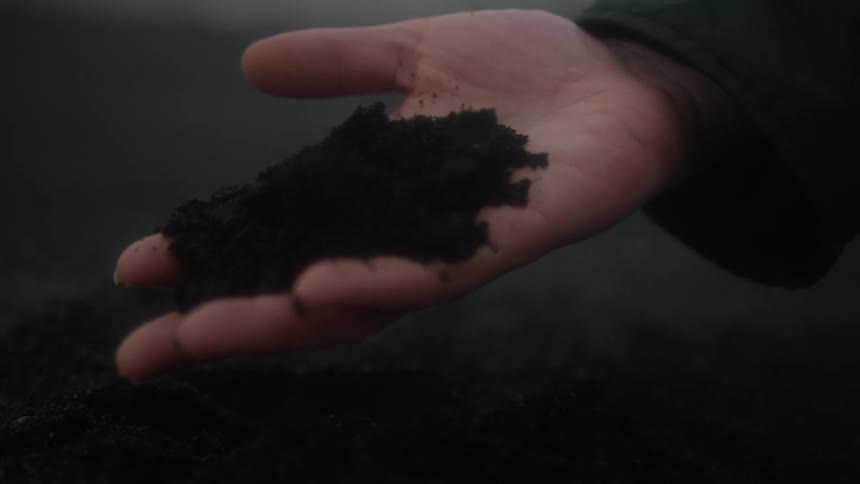 Close up on a hand stabbing black sand