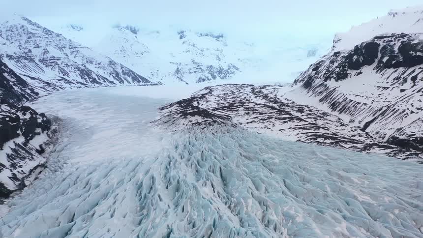 A region of the arctic with the ground covered in snow and there are some mountains around that are also white with snow on their surface