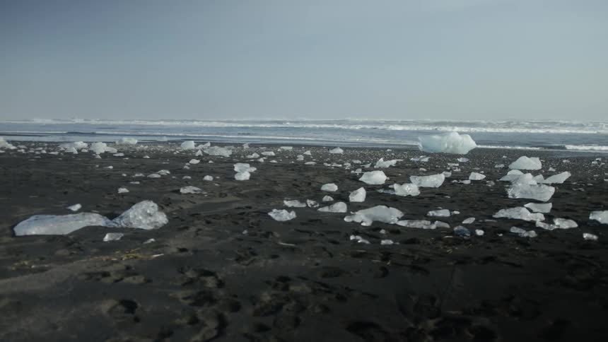 Black sand beach is covered with pieces of ice of various sizes contrasting with the sea in the background