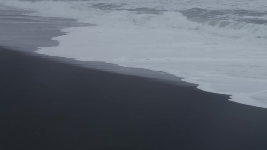 Waves flowing onto the beach from stormy seas foam on the sand