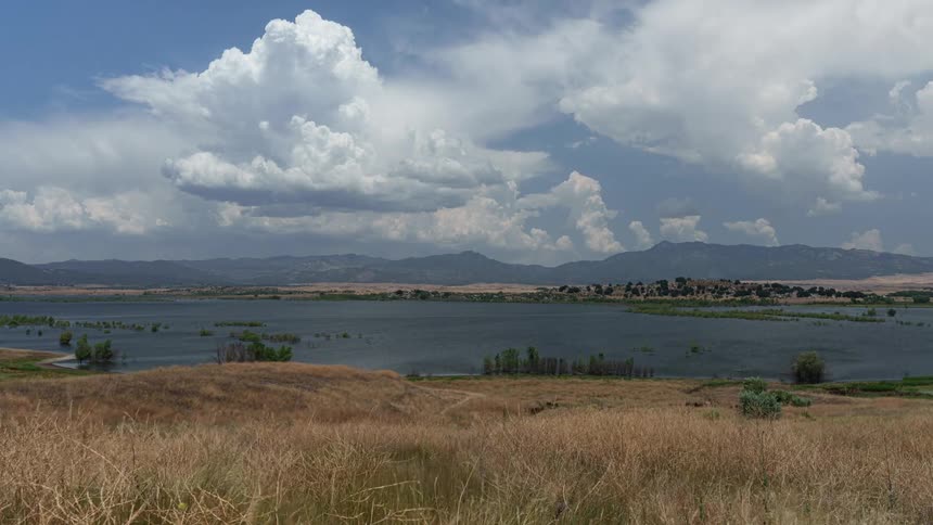Time lapse of wind rolling over a serene lake near the mountains under a partly cloudy sky