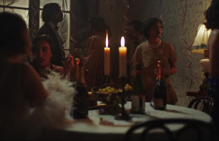 Men and women at a party in formal clothing with a central table with candles fruit wines and cocktails