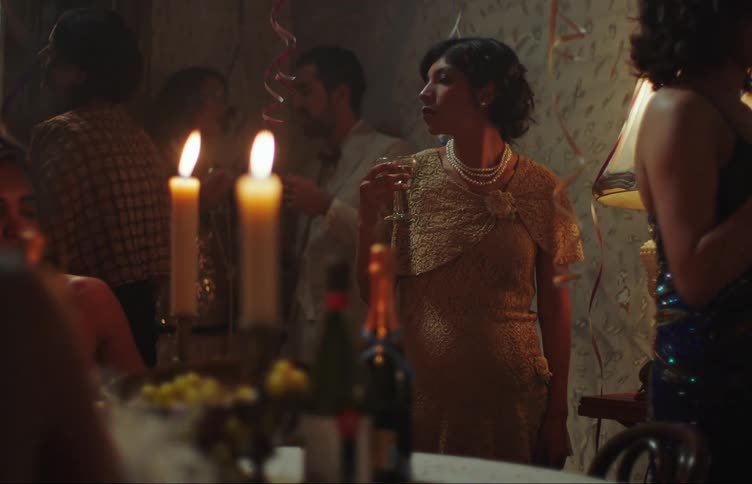 A woman standing in a place with several people talking and smoking and she drinks the drink that is in her hand